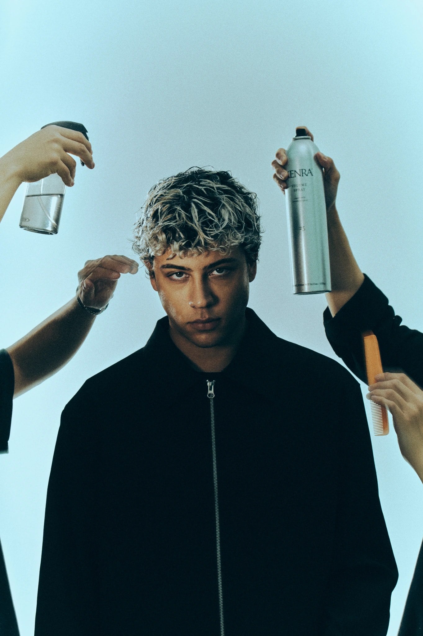 Bleached curls being styled on set, hands holding spray and comb